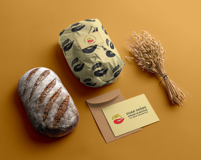 On a table there is a bread packed in a paper featuring Only grains logo, a bread, an envelope with a greeting card and grains