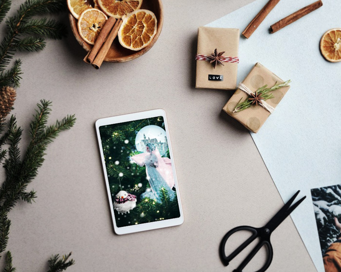 Christmas card mockup depicting The frozen kingdom presented on a tablet, placed on a flat surface between dried orange slices, Christmas tree branches, vanilla sticks, presents and a pair of scissors