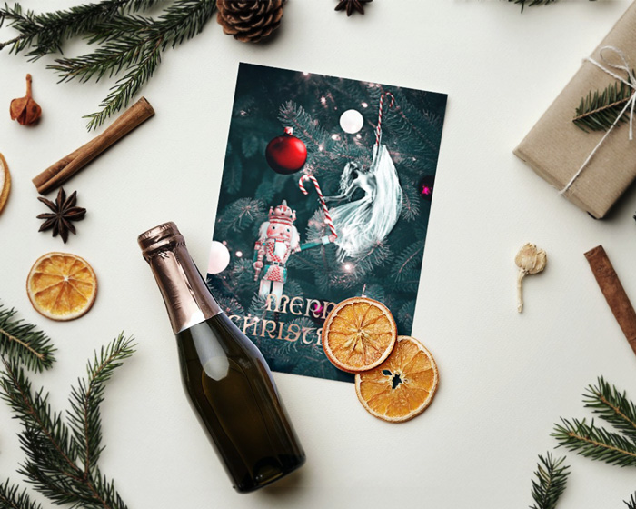 Christmas card mockup depicting a Christmas love story presented on a Christmas card, placed on a flat surface between dried orange slices, Christmas tree branches, pine cones, vanilla sticks, anise stars, presents and a Champaign bottle on top