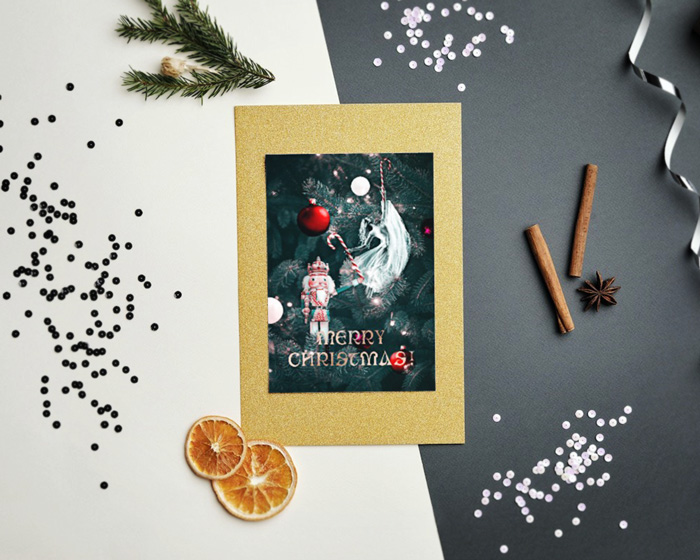 Christmas card mockup depicting a Christmas love story presented on a golden Christmas card, placed on a flat surface between dried orange slices, Christmas tree branches, vanilla sticks, anise stars and twine for presents