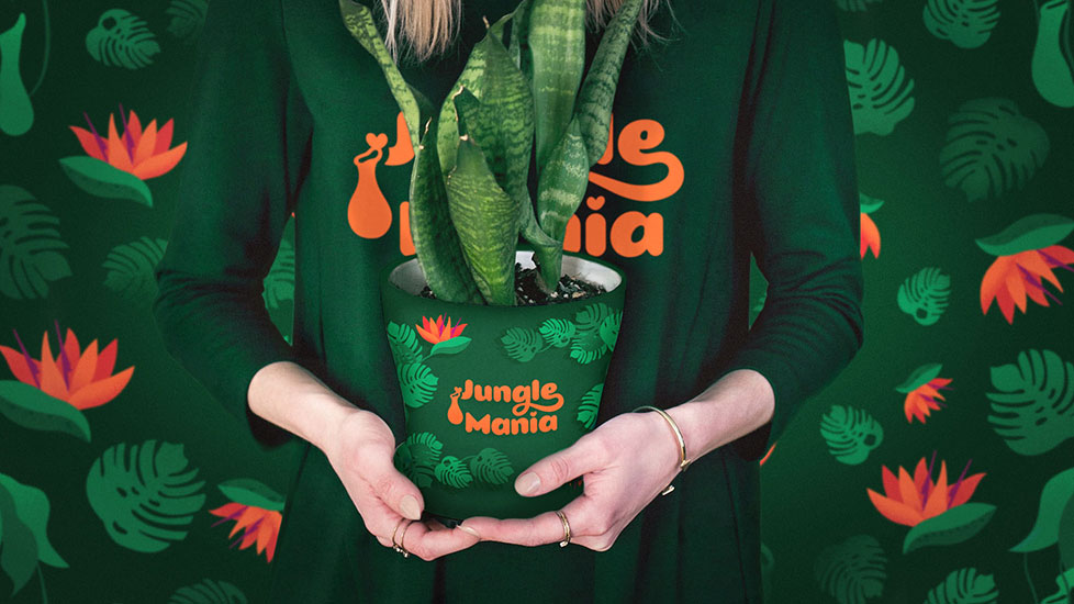 A girl wearing a shirt on which there is written the logotype of Jungle Mania is holding a snake plant in a pot. On the pot there is represented a tropical illustration depicting Monstera Deliciosa leaves and Bird of paradise flowers.
