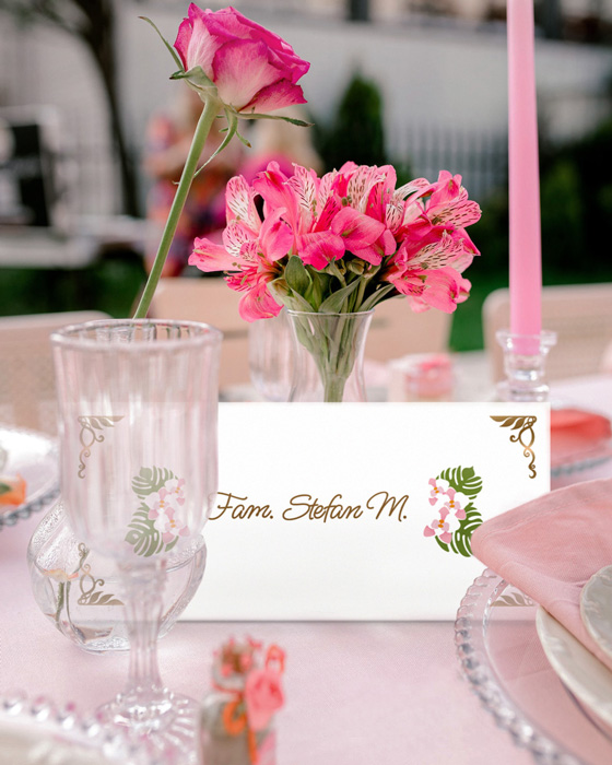 Mockup for Custom illustrated digital baptism pack depicting a guest name and gift envelope placed on a table in front of a flower vase. In front of the envelope there are a wine glass and a plate